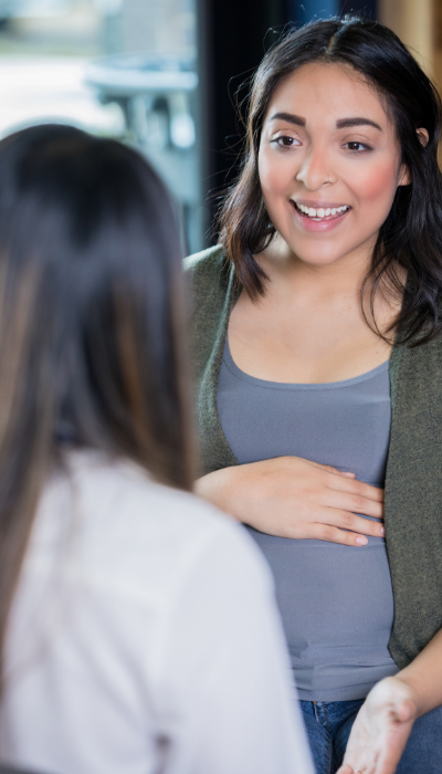 Image shows a pregnant woman, hand resting on her stomach, talking to her doula